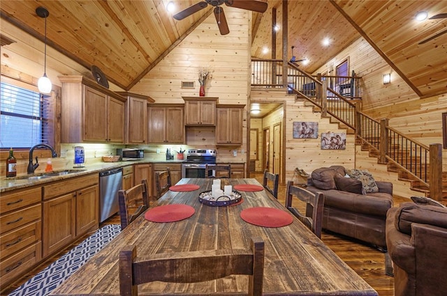 kitchen featuring appliances with stainless steel finishes, ceiling fan, wooden walls, pendant lighting, and high vaulted ceiling