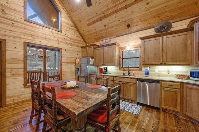 kitchen featuring stainless steel appliances, sink, high vaulted ceiling, hanging light fixtures, and wood walls