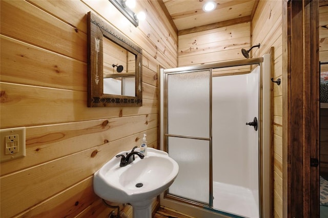 bathroom featuring walk in shower, wooden walls, and sink