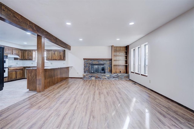 unfurnished living room with beamed ceiling, light hardwood / wood-style flooring, and a stone fireplace