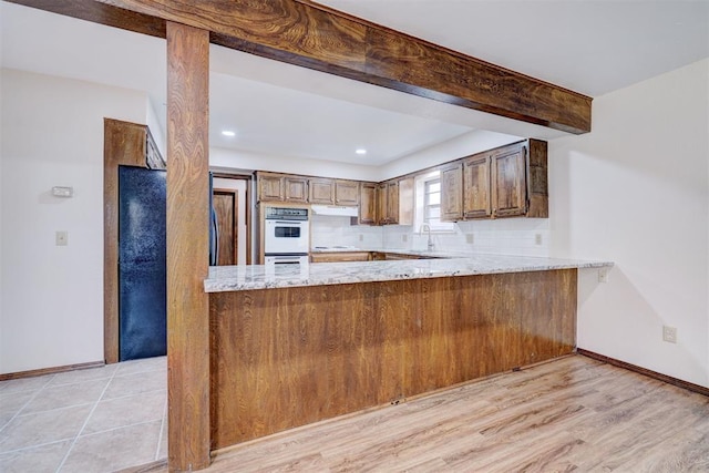 kitchen featuring white double oven, light wood-type flooring, tasteful backsplash, light stone counters, and kitchen peninsula