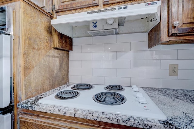 kitchen featuring decorative backsplash, light stone countertops, and white electric stovetop