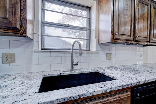 kitchen with dishwasher, sink, light stone counters, and dark brown cabinets