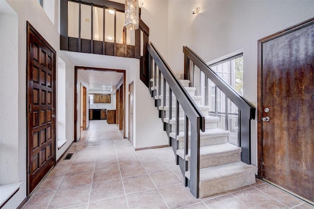 foyer entrance featuring stairs, a high ceiling, light tile patterned flooring, and visible vents