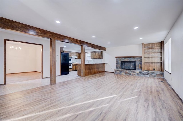 unfurnished living room with baseboards, light wood-style flooring, a stone fireplace, beam ceiling, and recessed lighting