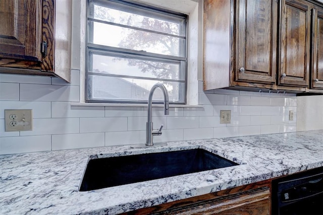 kitchen featuring black dishwasher, a sink, decorative backsplash, and dark brown cabinets