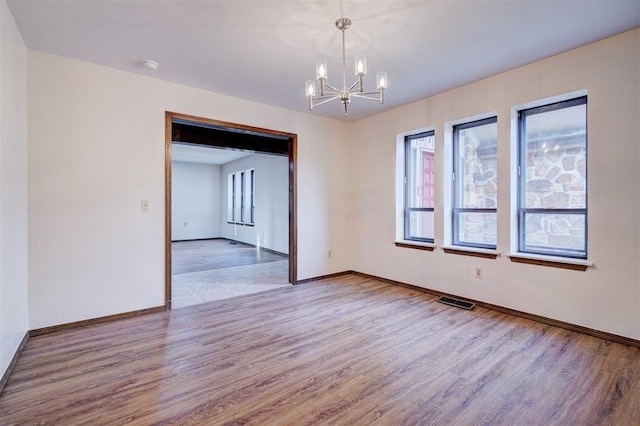 spare room with visible vents, a notable chandelier, baseboards, and wood finished floors