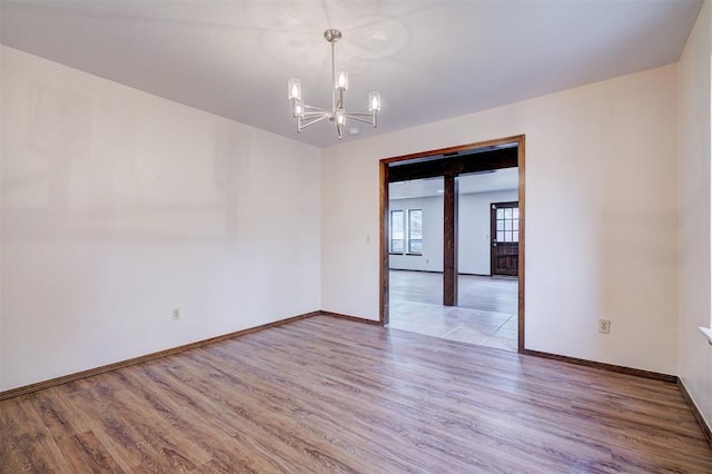 empty room featuring light wood-style flooring, baseboards, and a notable chandelier