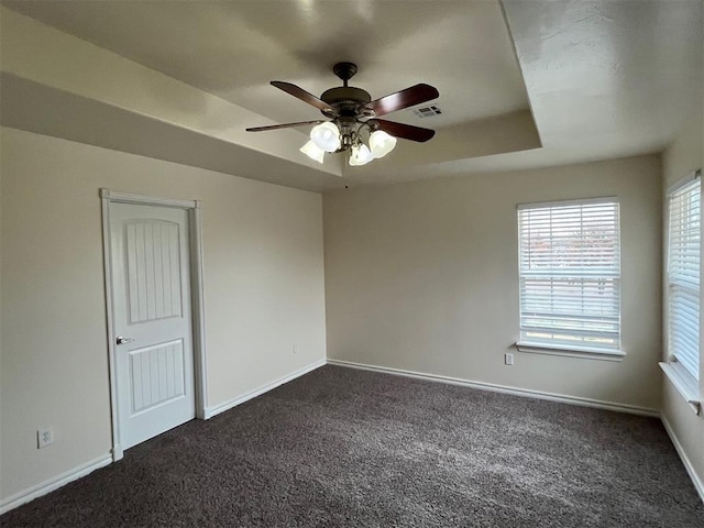 carpeted spare room featuring a raised ceiling and ceiling fan