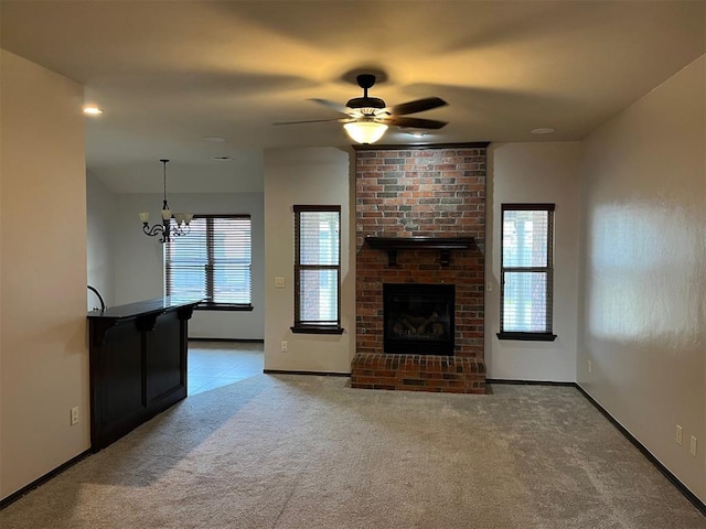 unfurnished living room featuring light colored carpet, ceiling fan with notable chandelier, and a brick fireplace