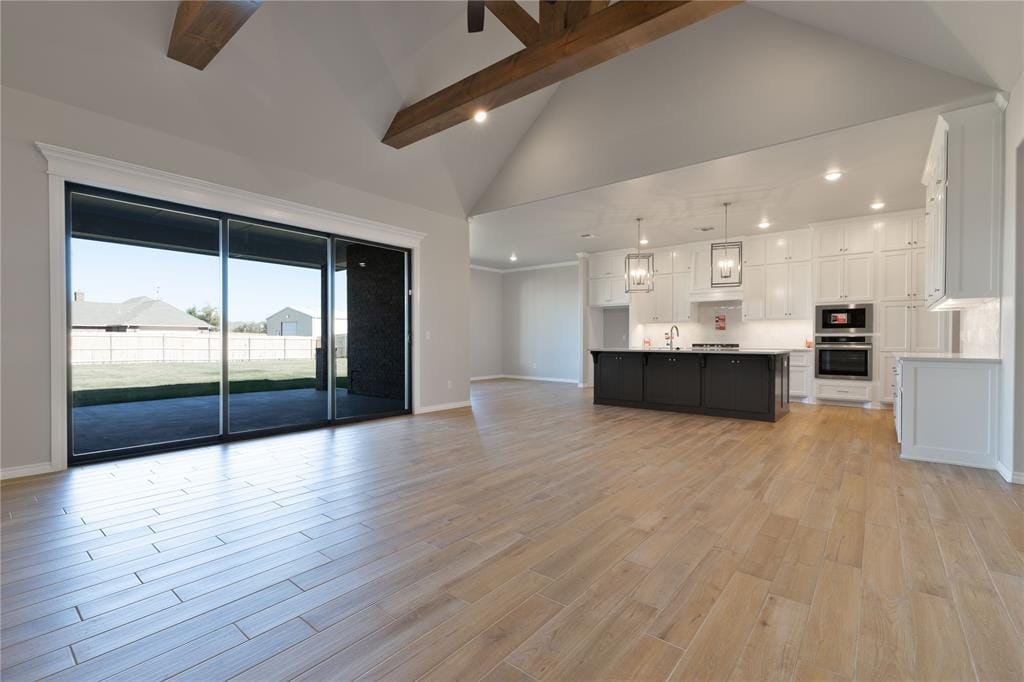 unfurnished living room with beam ceiling, light hardwood / wood-style floors, and high vaulted ceiling