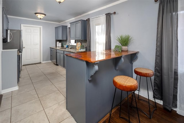 kitchen with stainless steel appliances, crown molding, gray cabinetry, a breakfast bar area, and sink