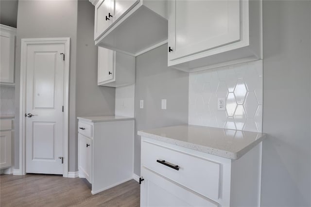 kitchen with light hardwood / wood-style floors, light stone countertops, white cabinetry, and backsplash