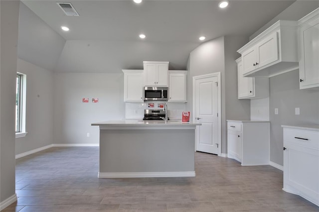 kitchen with white cabinetry, stainless steel appliances, an island with sink, and vaulted ceiling