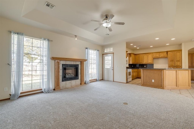 unfurnished living room with light carpet, a raised ceiling, and a wealth of natural light