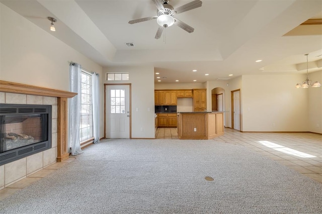 unfurnished living room featuring ceiling fan with notable chandelier, a raised ceiling, light tile patterned floors, and a fireplace