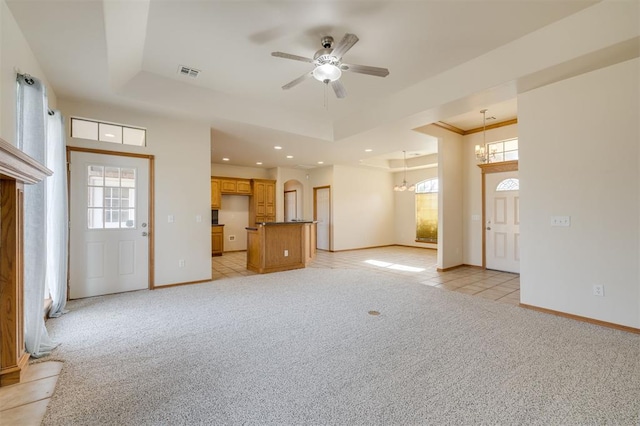 unfurnished living room featuring a raised ceiling, ceiling fan with notable chandelier, a healthy amount of sunlight, and light colored carpet