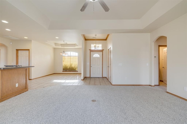 entrance foyer featuring ceiling fan with notable chandelier, light colored carpet, and a raised ceiling