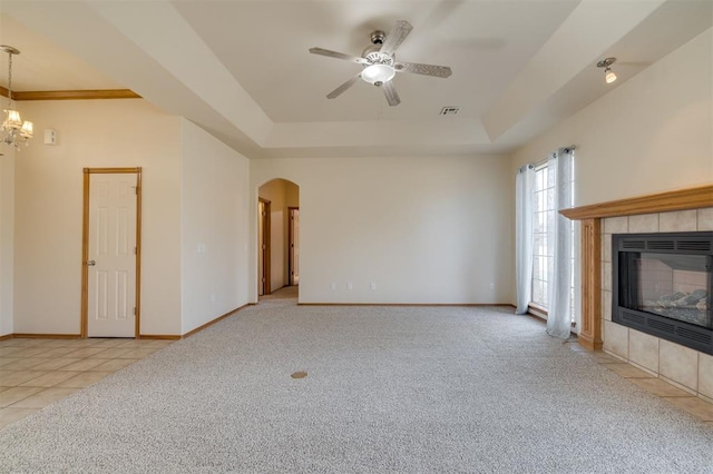 unfurnished living room featuring a tray ceiling, light carpet, a fireplace, and ceiling fan with notable chandelier