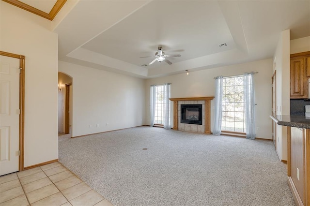 unfurnished living room with a raised ceiling, light carpet, a fireplace, and ceiling fan