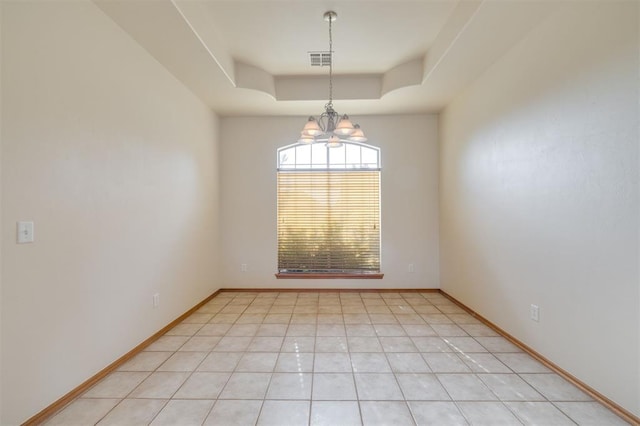 tiled spare room with a tray ceiling and a notable chandelier