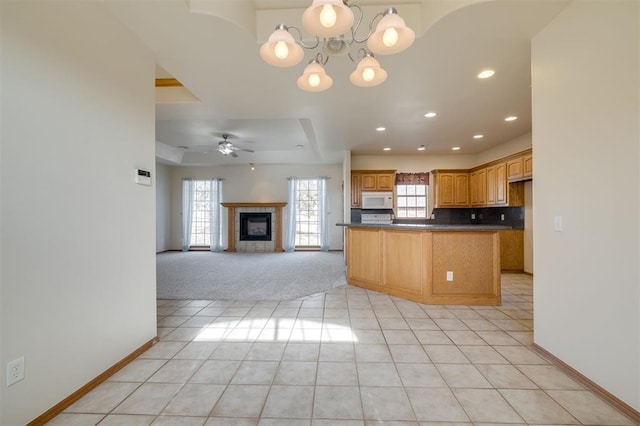 kitchen featuring kitchen peninsula, a tray ceiling, a tiled fireplace, decorative backsplash, and light tile patterned floors