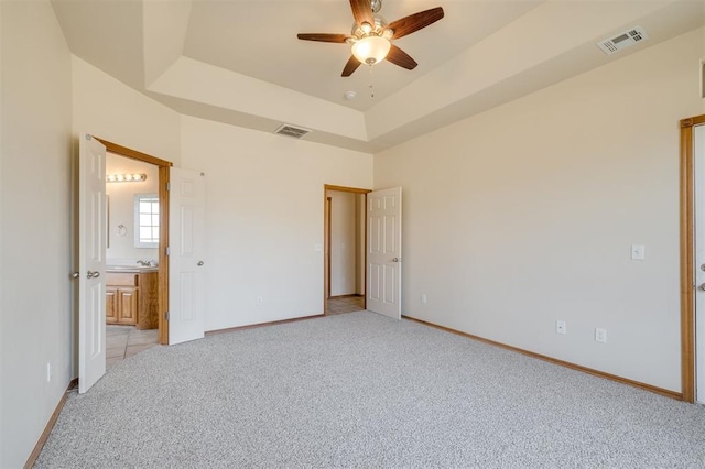 unfurnished bedroom featuring ensuite bathroom, ceiling fan, light carpet, and a tray ceiling