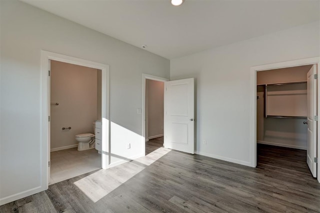 unfurnished bedroom featuring dark hardwood / wood-style flooring, ensuite bathroom, a spacious closet, and a closet