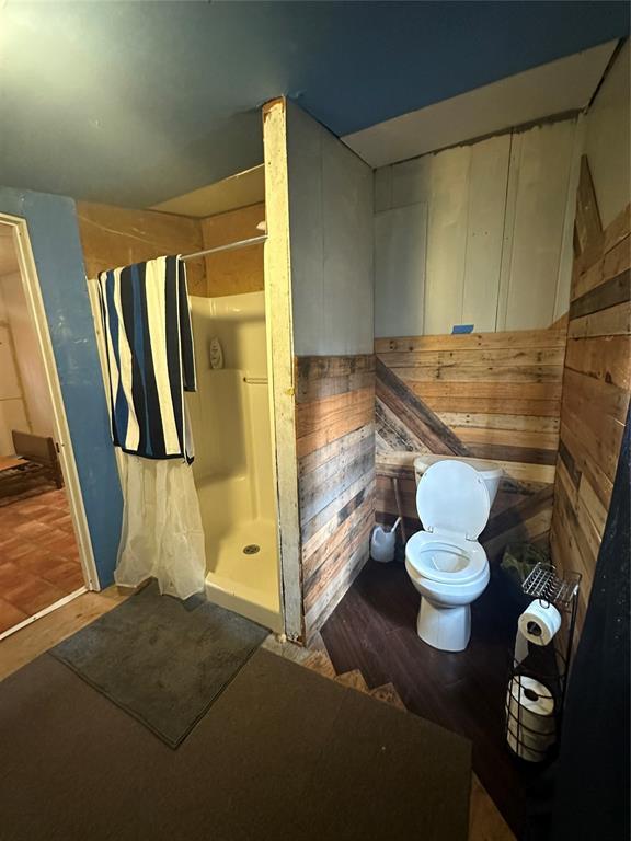 bathroom with a shower, wood-type flooring, toilet, and wood walls