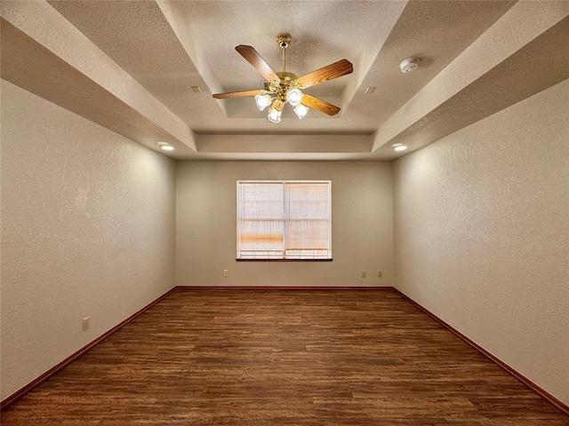 empty room featuring dark hardwood / wood-style floors, ceiling fan, a textured ceiling, and a tray ceiling