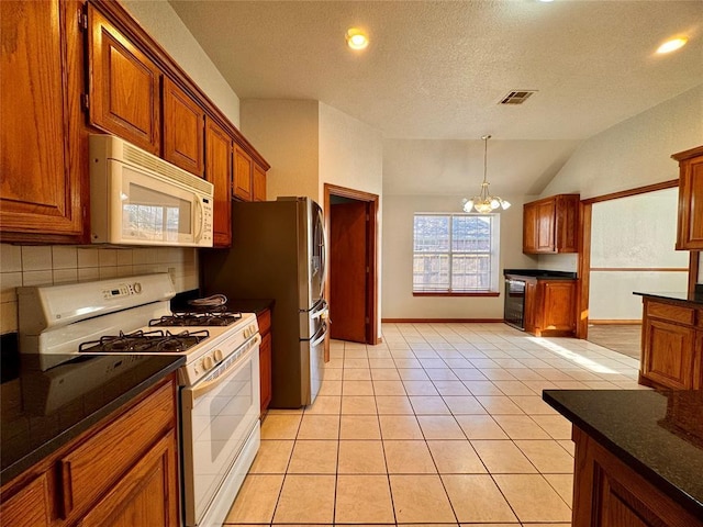 kitchen featuring a textured ceiling, white appliances, an inviting chandelier, lofted ceiling, and light tile patterned flooring