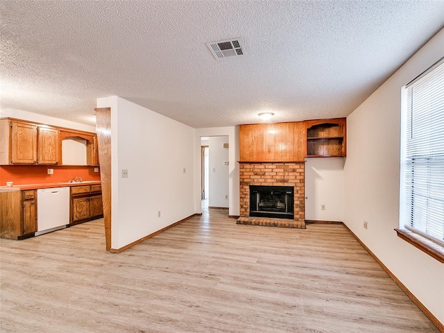 unfurnished living room with a textured ceiling, light hardwood / wood-style floors, a brick fireplace, and plenty of natural light