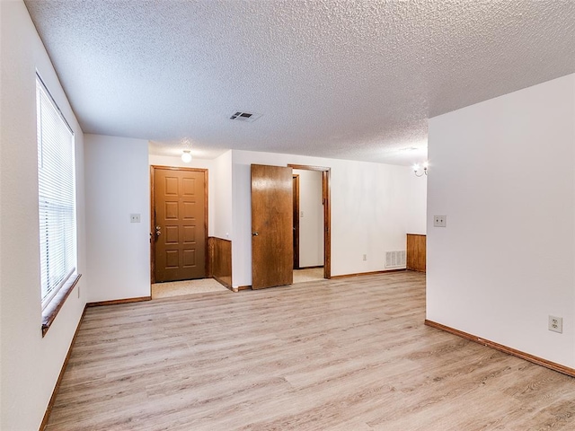 unfurnished room with light hardwood / wood-style floors, a textured ceiling, and an inviting chandelier