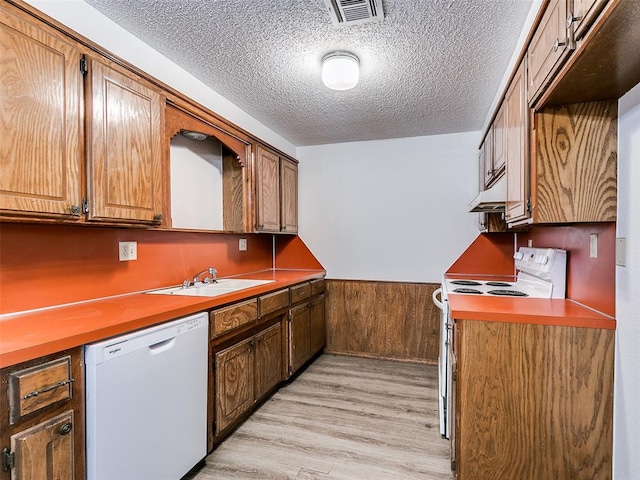 kitchen featuring sink, wood walls, light hardwood / wood-style floors, a textured ceiling, and white appliances