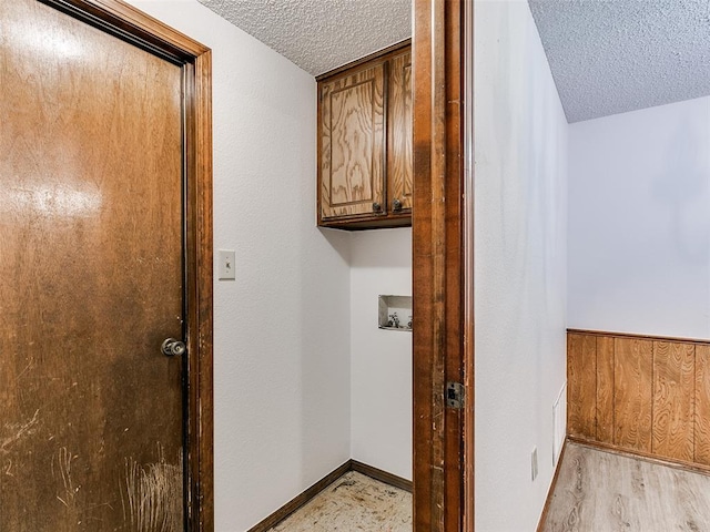 laundry area featuring cabinets, wooden walls, hookup for a washing machine, light hardwood / wood-style flooring, and a textured ceiling