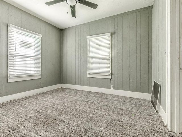 carpeted empty room featuring heating unit, wooden walls, and ceiling fan