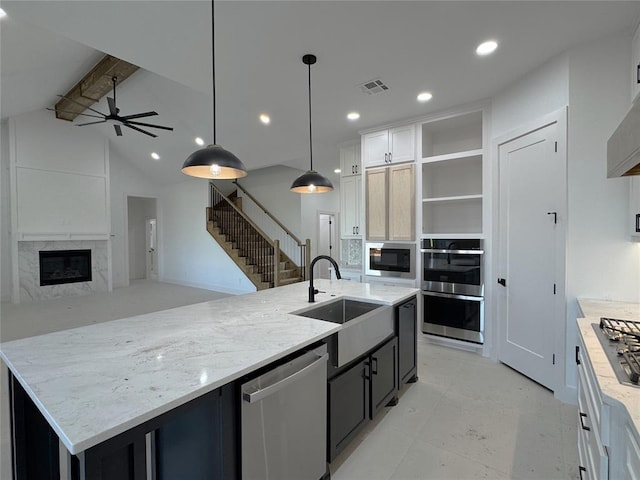 kitchen featuring hanging light fixtures, stainless steel appliances, light stone countertops, an island with sink, and white cabinets