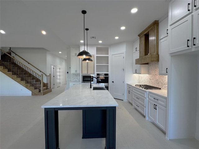 kitchen with pendant lighting, sink, light stone countertops, white cabinets, and a center island with sink