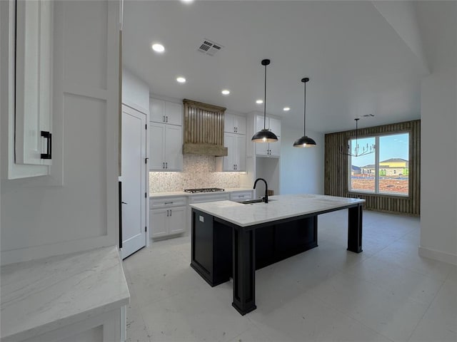 kitchen featuring sink, decorative light fixtures, a center island with sink, light stone countertops, and white cabinets