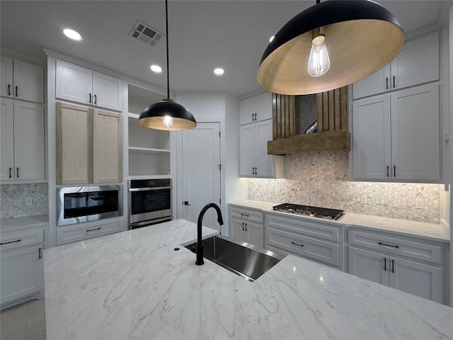 kitchen featuring sink, white cabinetry, stainless steel appliances, light stone countertops, and decorative light fixtures