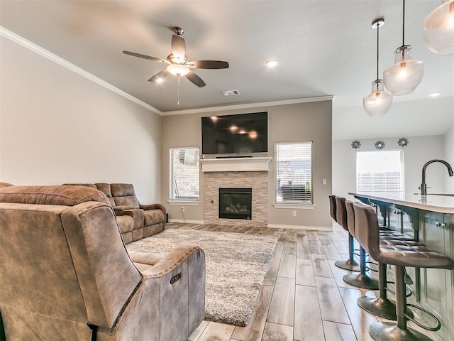 living room featuring sink, crown molding, ceiling fan, light wood-type flooring, and a fireplace