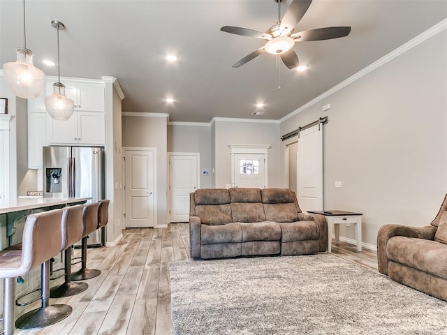 living room with a barn door, ceiling fan, ornamental molding, and light wood-type flooring