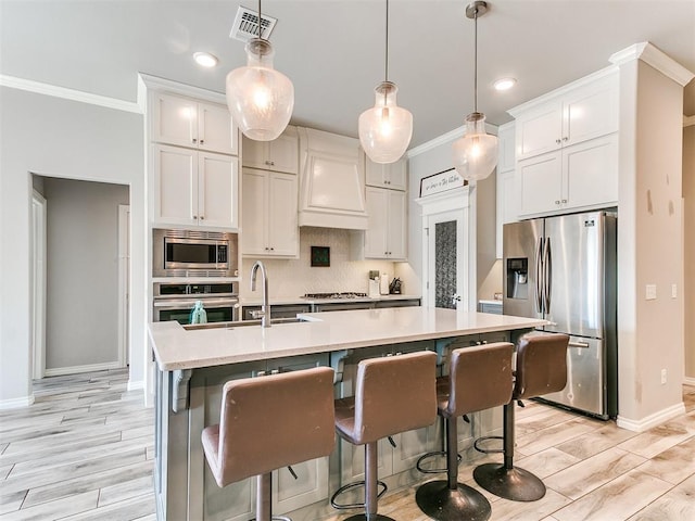 kitchen featuring an island with sink, stainless steel appliances, white cabinetry, and custom exhaust hood