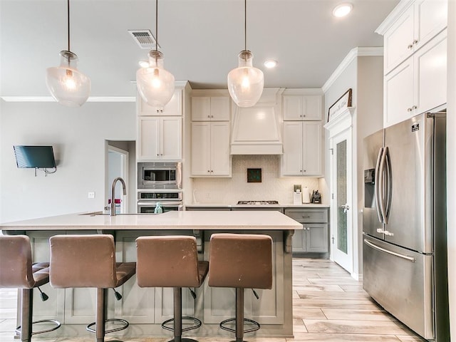 kitchen with decorative light fixtures, light wood-type flooring, stainless steel appliances, and an island with sink