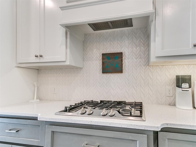 kitchen featuring stainless steel gas stovetop, backsplash, exhaust hood, white cabinets, and light stone countertops