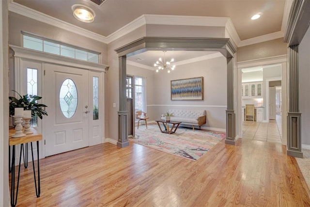 foyer entrance with ornate columns, crown molding, a notable chandelier, and light wood-type flooring