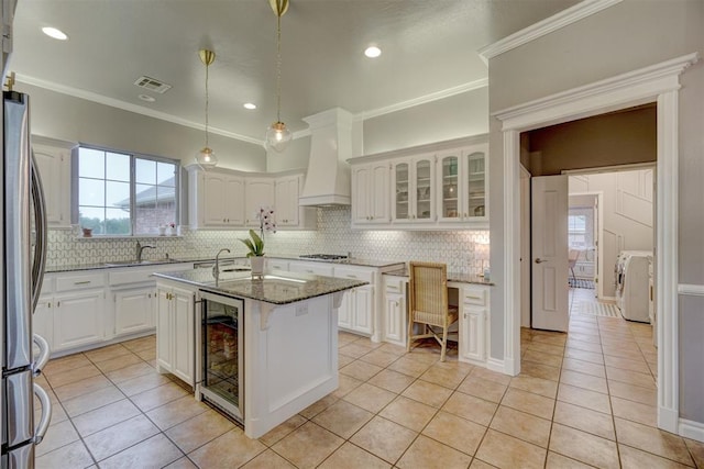 kitchen with dark stone countertops, a center island with sink, white cabinets, custom exhaust hood, and appliances with stainless steel finishes