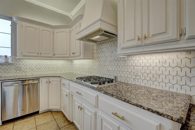 kitchen with crown molding, dark stone countertops, custom range hood, white cabinetry, and stainless steel appliances