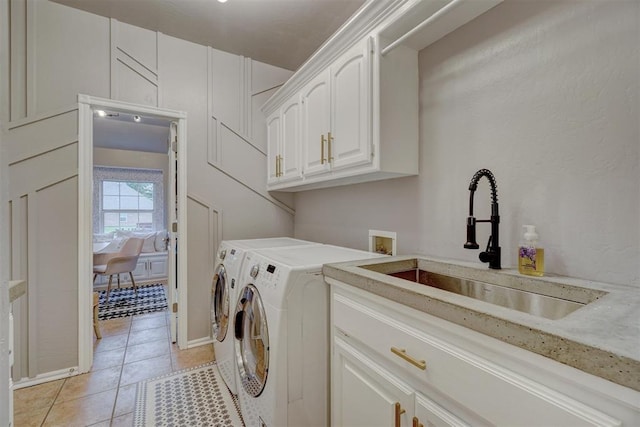 clothes washing area with washing machine and dryer, sink, light tile patterned floors, and cabinets