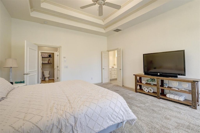 bedroom with a raised ceiling, crown molding, ceiling fan, connected bathroom, and light colored carpet